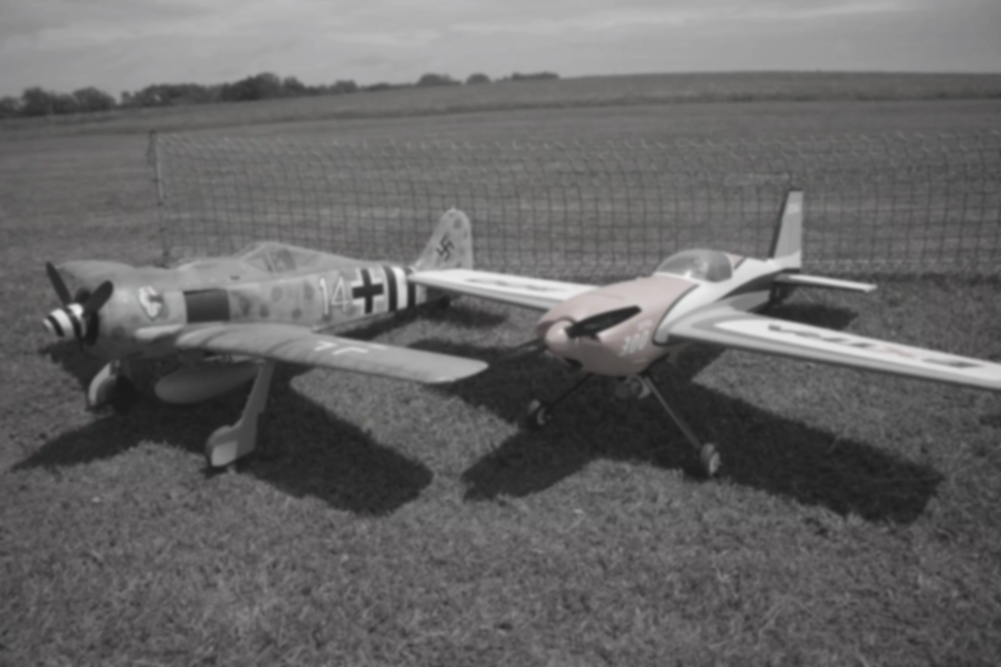 Dvě letadla sedící na zemi. Jedno německé bojové útočné letadlo a druhé akrobatické RC letadlo.